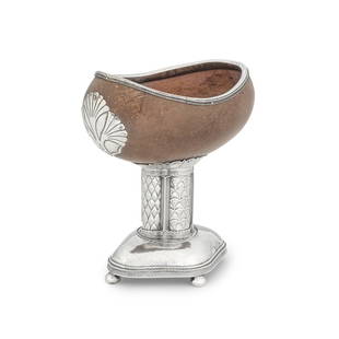 An Arts and Crafts silver-mounted coconut cup John Paul Cooper, London 1926: An Arts and Crafts silver-mounted coconut cup John Paul Cooper, London 1926 A sideways hollowed out polished coconut, surmounted by a silver double rope-twist rim, to one end a chased and pinned silv