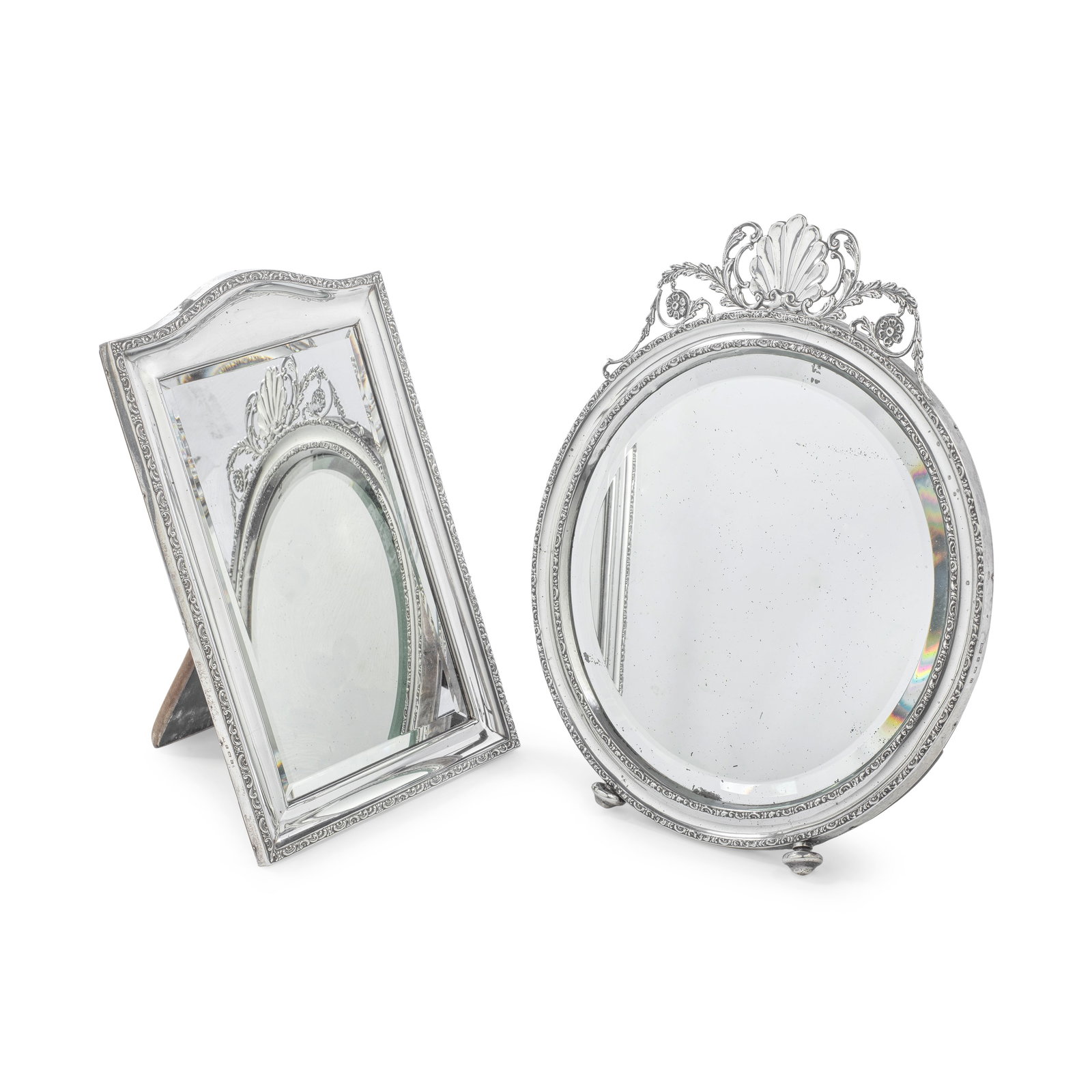 Two silver table mirrors both Henry Matthews, Birmingham 1913 and Birmingham 1909 (2): Two silver table mirrors both Henry Matthews, Birmingham 1913 and Birmingham 1909 The first, circular, the concave border between two narrow scroll rims, shell and foliate scroll surmount, on bun fee