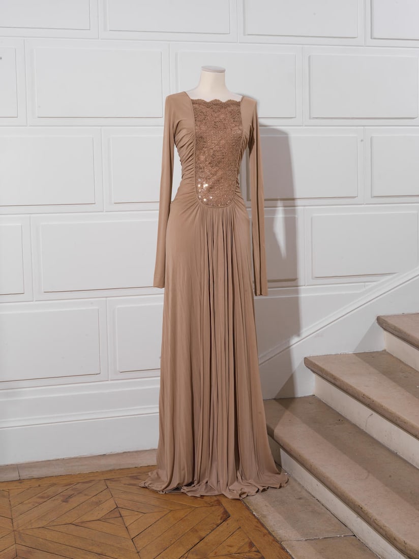 Guy LAROCHE Collection. Robe longue jersey beige.: Guy LAROCHE Collection. Robe longue jersey beige. Encolure bateau sur important empiècement en dentelle brodée de sequins, manches longues, jupe évasée. Griffe beige, graphisme noi