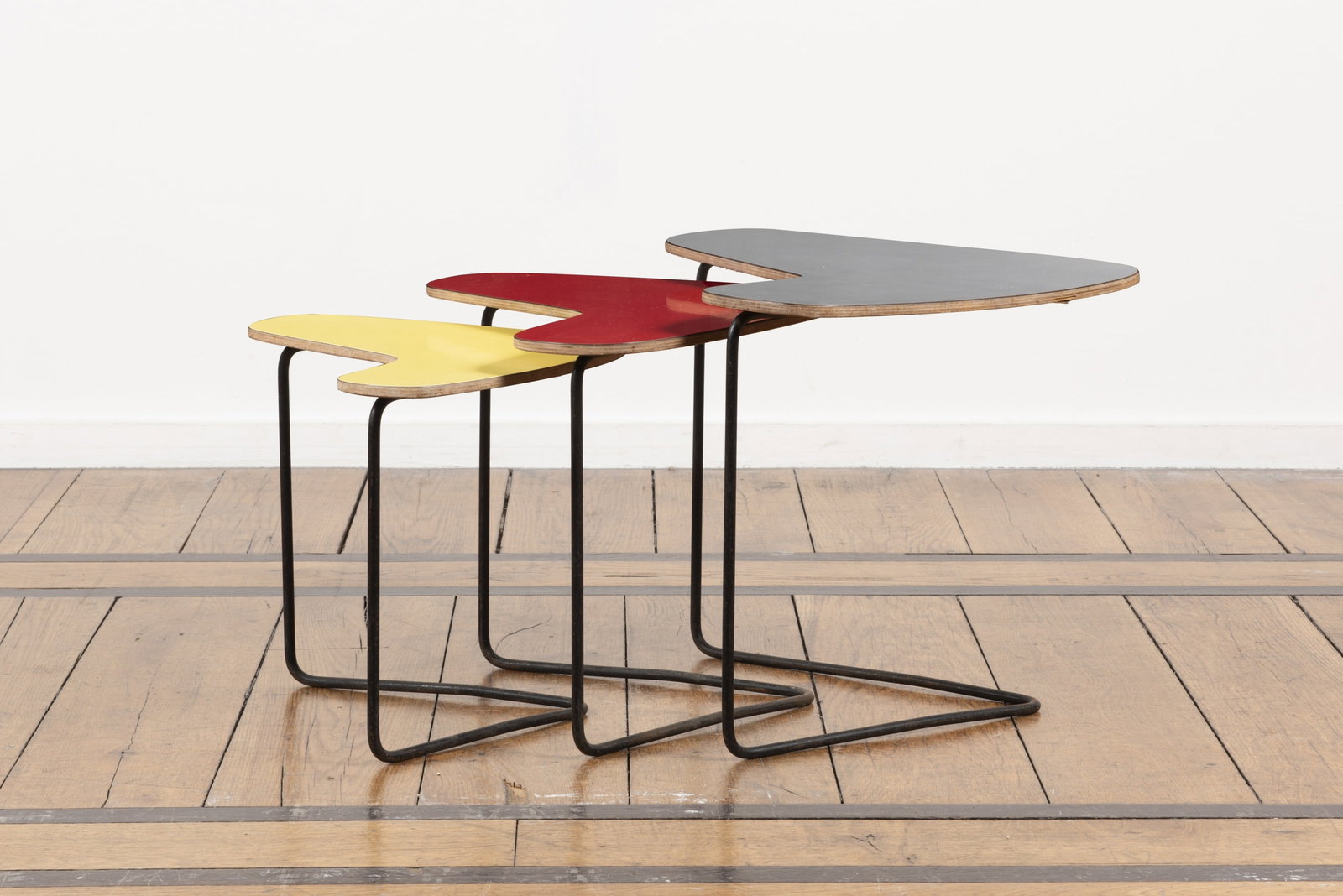 WILLY VAN DER MEEREN (1923-2002): WILLY VAN DER MEEREN (1923-2002) Trois tables gigognes à plateaux boomerang en contreplaqué, stratifié gris, rouge et jaune sur piètements en fil de métal laqué noir Tuba