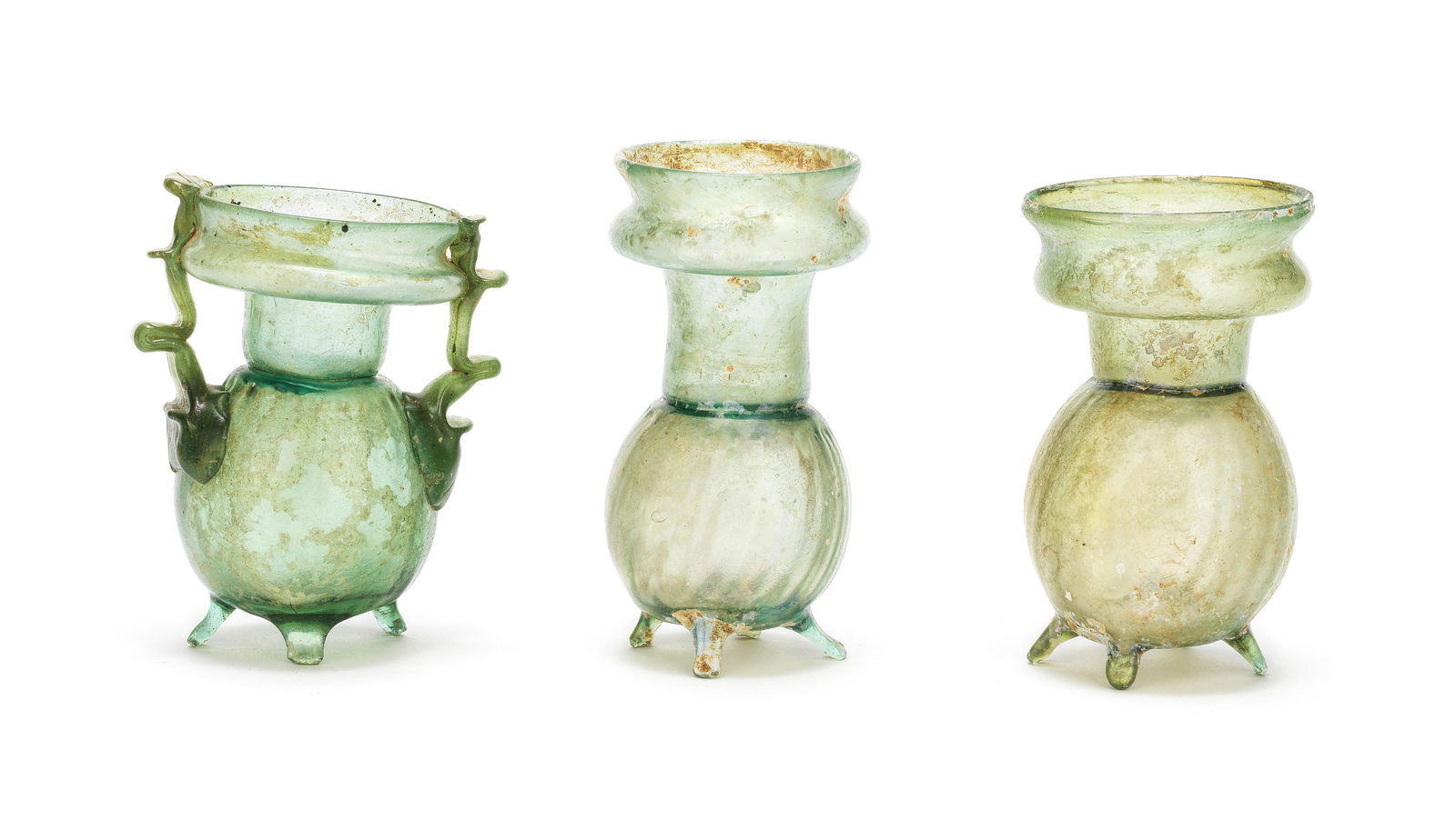 Three Roman green glass footed sprinkler flasks 3: Three Roman green glass footed sprinkler flasks Circa 4th Century A.D. 9.8cm, 9.2cm and 9.1cm high (3) Footnotes: Provenance: Anonymous sale; Pierre Bergé & Associés, Paris, 5 June 2009, l
