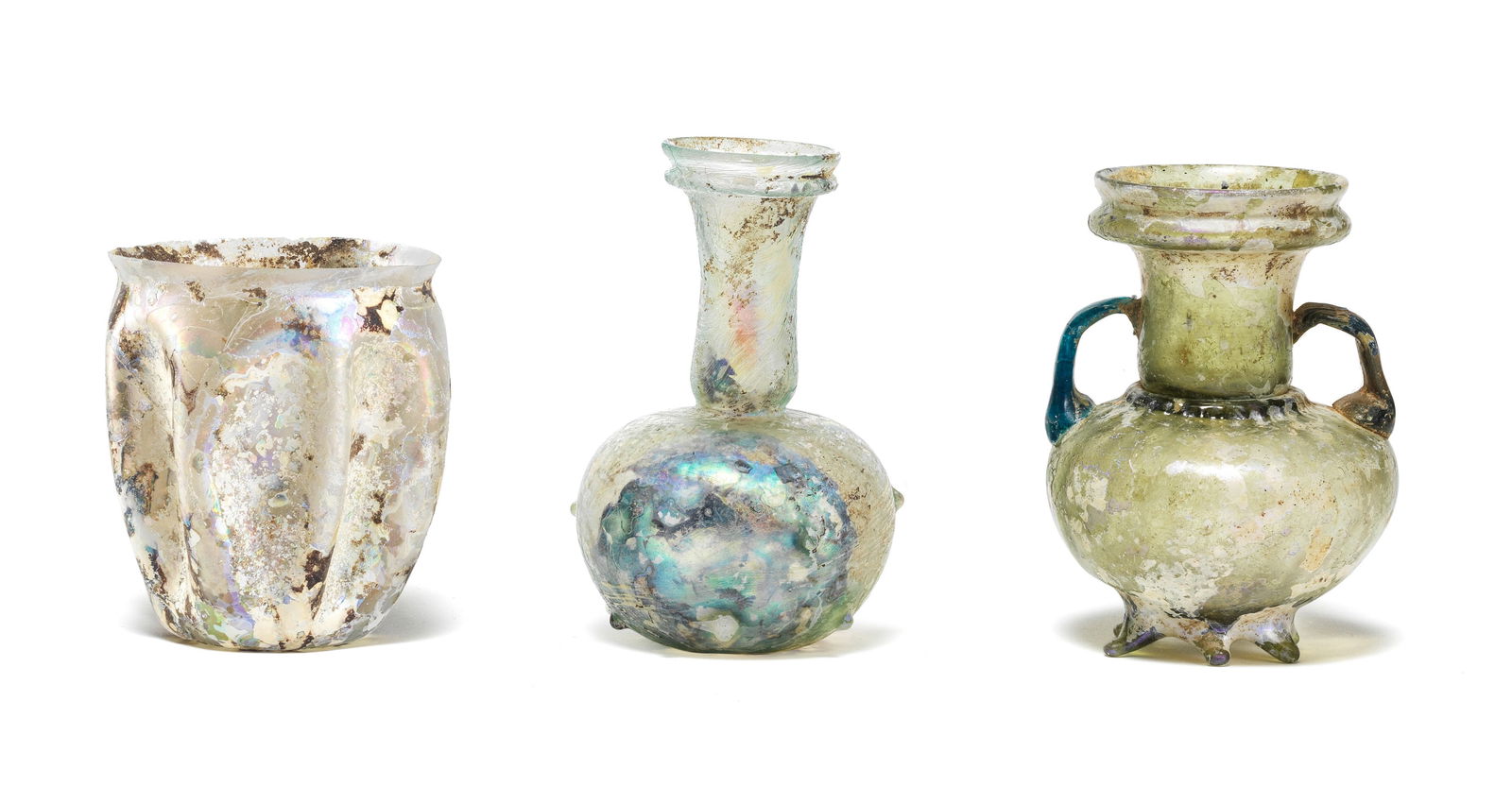A Roman green glass sprinkler flask, a Roman pale blue-green glass flask, and a Roman colourless...: A Roman green glass sprinkler flask, a Roman pale blue-green glass flask, and a Roman colourless glass beaker Circa 1st-4th Century A.D. 9.5cm, 10.2cm and 7.8cm high (3) Footnotes: Provenance: Spr