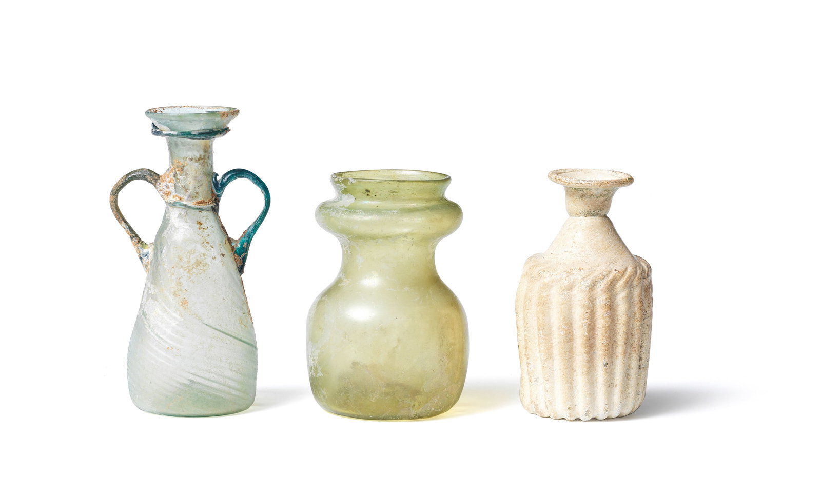 A Roman green glass double-handled conical flask, a Roman green glass ribbed sprinkler flask, a ...: A Roman green glass double-handled conical flask, a Roman green glass ribbed sprinkler flask, a Roman yellow-green glass jar, and a Roman blue-green glass feeder vessel Circa 2nd-5th Century A.D. con