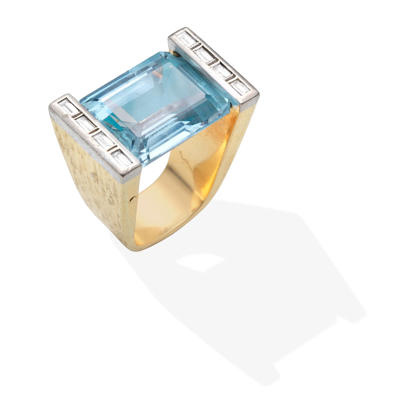 GRIMA: TOPAZ AND DIAMOND RING,: GRIMA: TOPAZ AND DIAMOND RING, CIRCA 1990 Bicoloured, the step-cut blue topaz between baguette-cut diamonds, in textured mount, topaz damaged, mount possibly with later modifications, topaz very appro