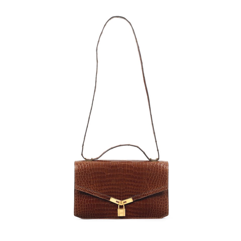 Hermès: a Shiny Miel Porosus Crocodile Cadena Lock Shoulder Bag 1979: Hermès: a Shiny Miel Porosus Crocodile Cadena Lock Shoulder Bag 1979 Shiny brown crocodile flap bag with a gold tone Kelly lock fastening and hardware Condition Grade C+ 25cm wide, 15cm high, 3cm