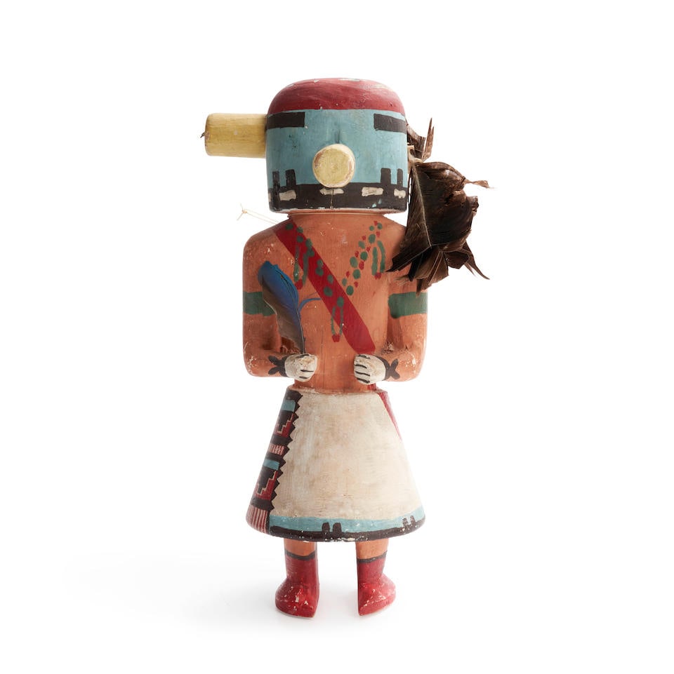A Hopi katsina doll ht. 13 1/4 in.: A Hopi katsina doll Carved from heavy wood, wearing a white kilt with painted sash, orange shirt, the blue and red head with a round orange snout. ht. 13 1/4 in. For further information on this lot pl