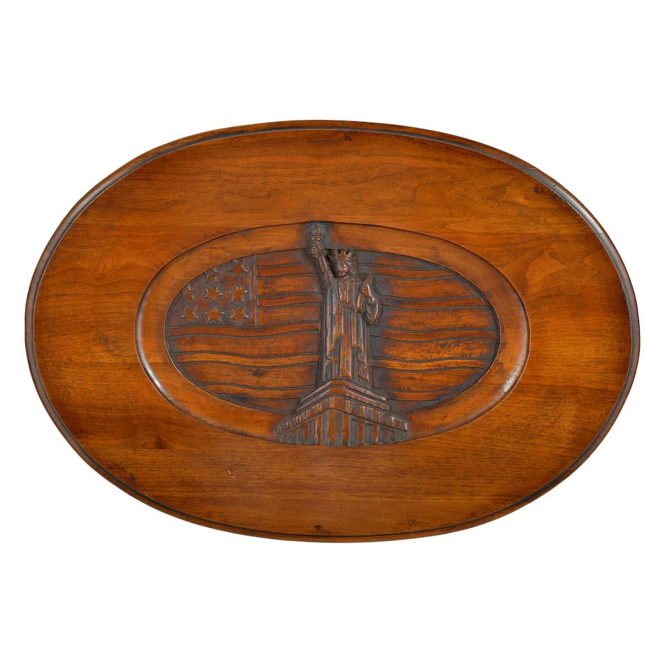 RELIEF PLAQUE OF THE STATUE OF LIBERTY: RELIEF PLAQUE OF THE STATUE OF LIBERTY United States of America, c. 1950, oval mahogany oval tabletop intaglio carved to depict the Statue of Liberty in front of the U.S. flag, 71cm wide, 7cm deep, 48