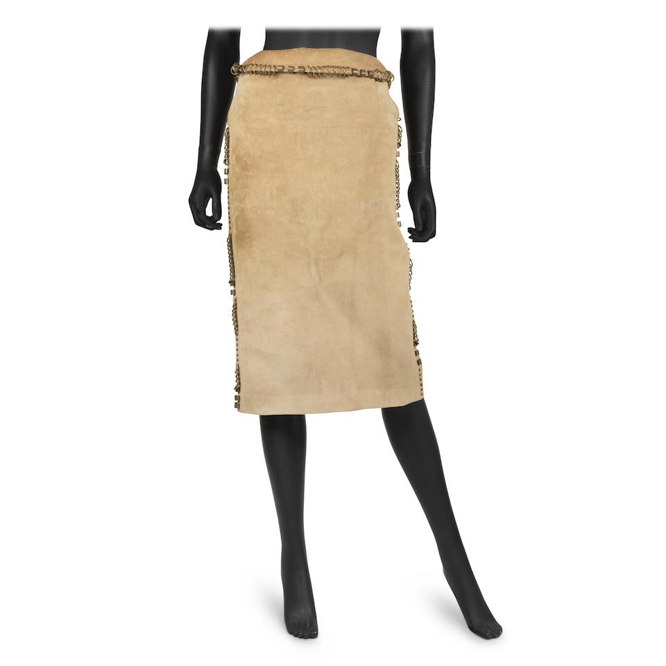 Yves Saint Laurent: a Tan Suede Skirt Mombasa Collection, Spring/Summer 2002: Yves Saint Laurent: a Tan Suede Skirt Mombasa Collection, Spring/Summer 2002 Creative Director: Tom Ford Runway look 21 Below the knee length skirt with bronze metal loop detailing to waist and sides