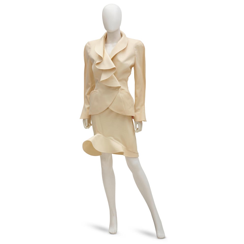 THIERRY MUGLER: SCALLOPED SKIRT SUIT ENSEMBLE Fall/Winter 1989: THIERRY MUGLER: SCALLOPED SKIRT SUIT ENSEMBLE Fall/Winter 1989 • Ivory Wool Scalloped Detail on Exterior • Snap Button Closure • Marked Size 38 Footnotes: OVERALL CONDITION: Good | S