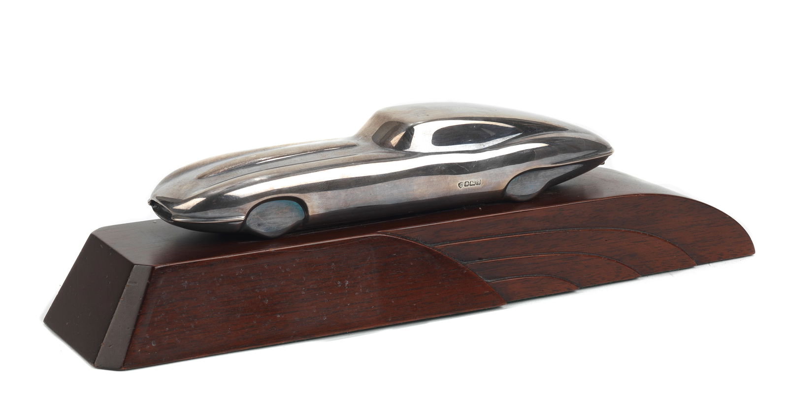 A streamlined sterling silver model of a Jaguar E-Type, British, 1998,: A streamlined sterling silver model of a Jaguar E-Type, British, 1998, by Jack Spencer, hallmarked Sheffield 1998, 20.5cm long, mounted on a shaped mahogany base, 32cm long overall.