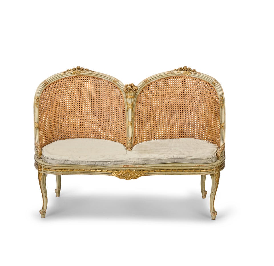 A French late 19th century painted and parcel gilt caned canape or conversation seat 1875-1890, ...: A French late 19th century painted and parcel gilt caned canape or conversation seat 1875-1890, in the Louis XV/XVI Transitional style Of serpentine outline, the double caned back of twin arched form
