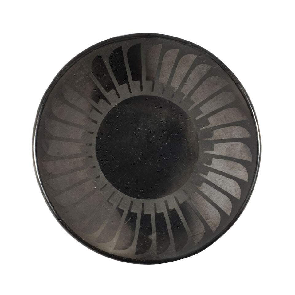 A Maria Martinez and Popovi Da feather-motif plate: Maria Martinez and Popovi Da San Ildefonso Pueblo, (1887-1980) and (1923-1971), a blackware plate with feather border, signed verso: Maria / Popovi. height 1in, diameter 5 7/8in Footnotes: Provenance
