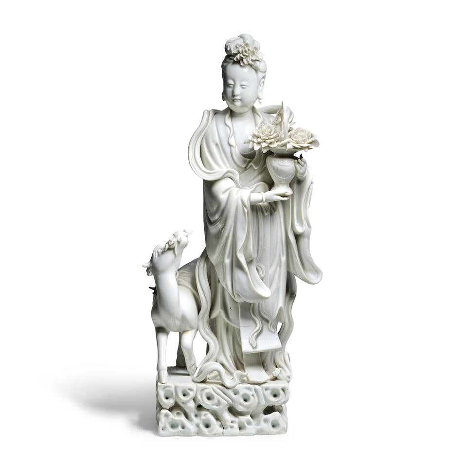 A BLANC-DE-CHINE FIGURE OF MAGU AND DEER 19th century (2): A BLANC-DE-CHINE FIGURE OF MAGU AND DEER 19th century The Immortal dressed in a long wind-swept robe with a ribbon draped around her, holding an amphora vase issuing blossoms, her face with serene exp