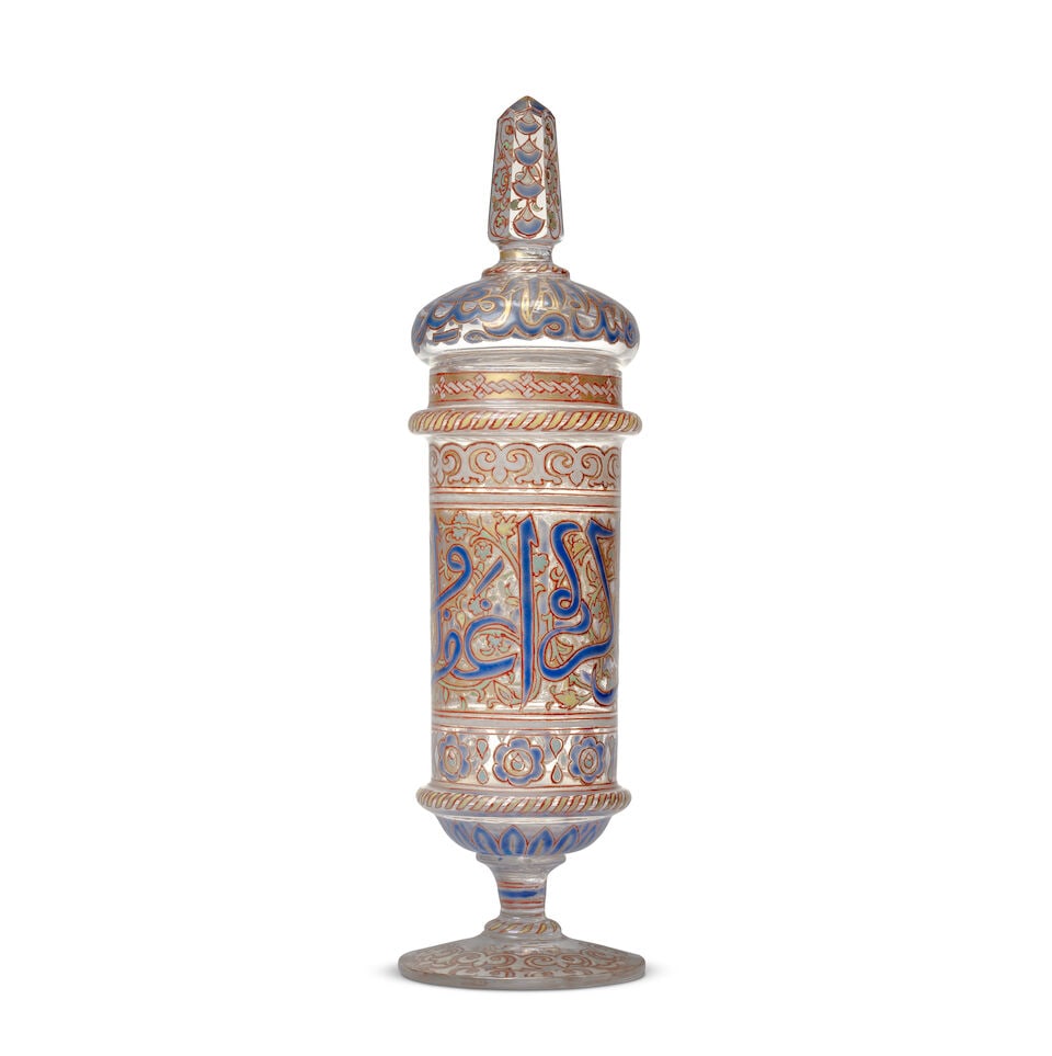 A Mamluk style enamelled glass goblet Europe, Late 19th/ early 20th Century: A Mamluk style enamelled glass goblet Europe, Late 19th/ early 20th Century of cylindrical form on a stemmed foot, the domed lid with hexagonal glass finial, decorated in polychrome enamel and gilt wi