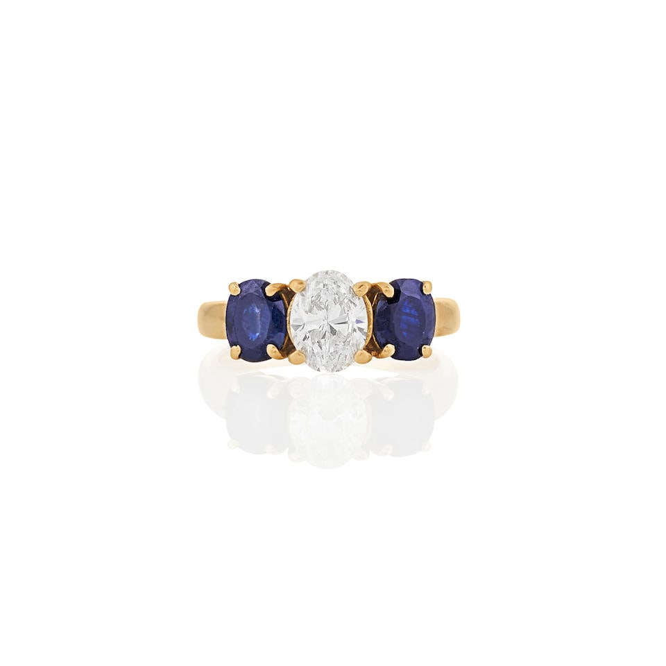 AN 18K GOLD, SAPPHIRE, AND DIAMOND RING: AN 18K GOLD, SAPPHIRE, AND DIAMOND RING Centering an oval-cut laser drilled diamond weighing 0.90 carats, flanked by fancy-cut sapphires, each measuring approximately 5.95 x 4.85 x 2.60 mm, size 5. Fo