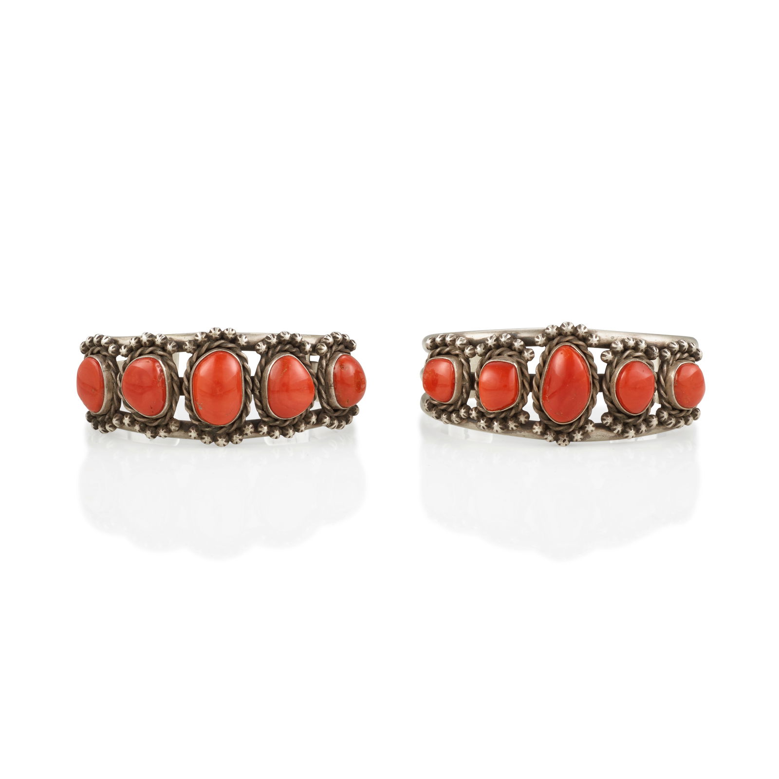 Two silver and coral cuff bracelets: Two silver and coral cuff bracelets Each constructed from a trio of domed wires supporting five graduated coral stones within twisted wire and silver drop surrounds, each indistinctly signed *** Thoma