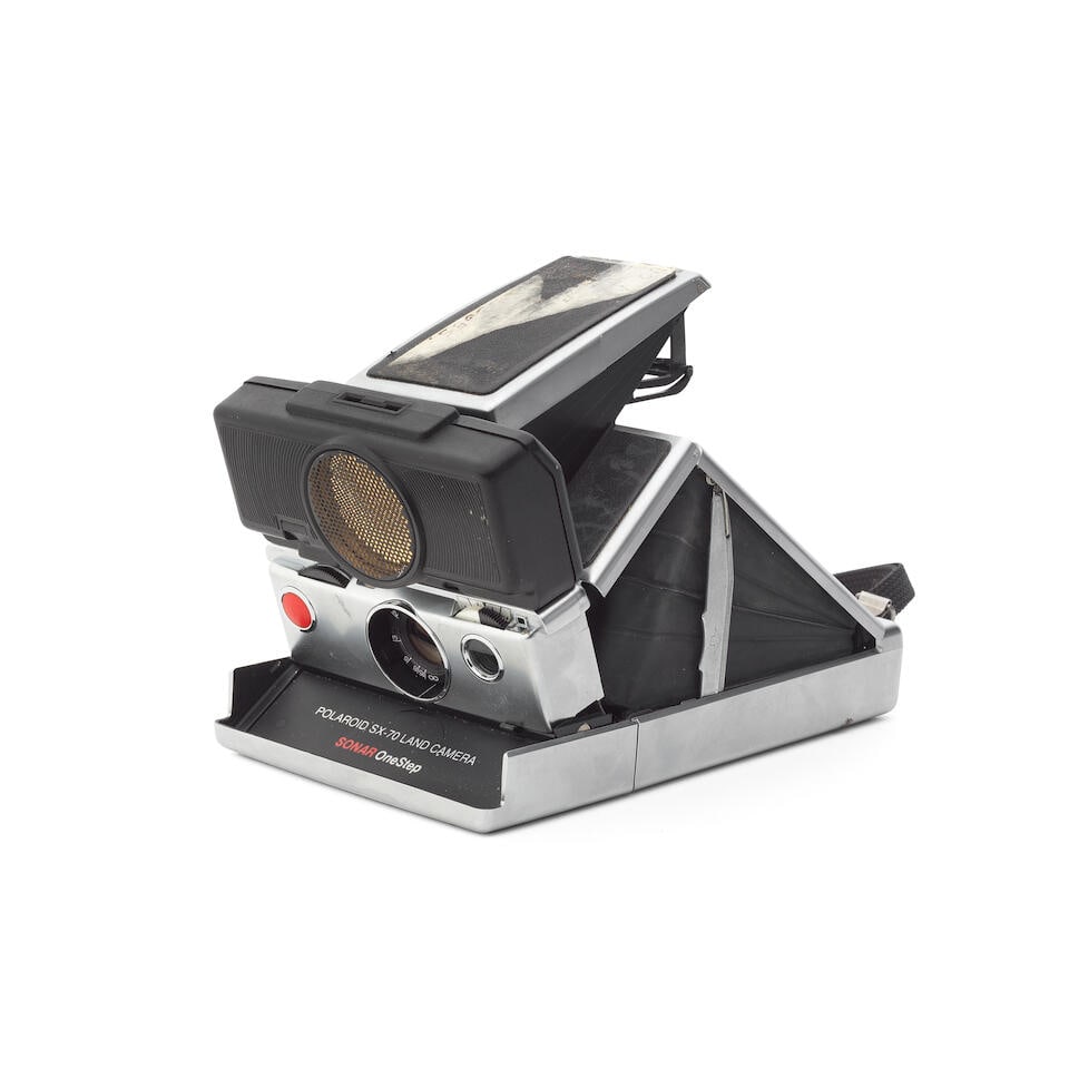 Brian Duffy (1933-2010): The Sonar OneStep Polaroid SX-70 Land Camera used on the Lodger shoot, ...: Brian Duffy (1933-2010): The Sonar OneStep Polaroid SX-70 Land Camera used on the Lodger shoot, 1970s, Made in USA, red shutter button, instructions to back, with strap, flat 9 x 4 1/4in (23 x 11cm) F