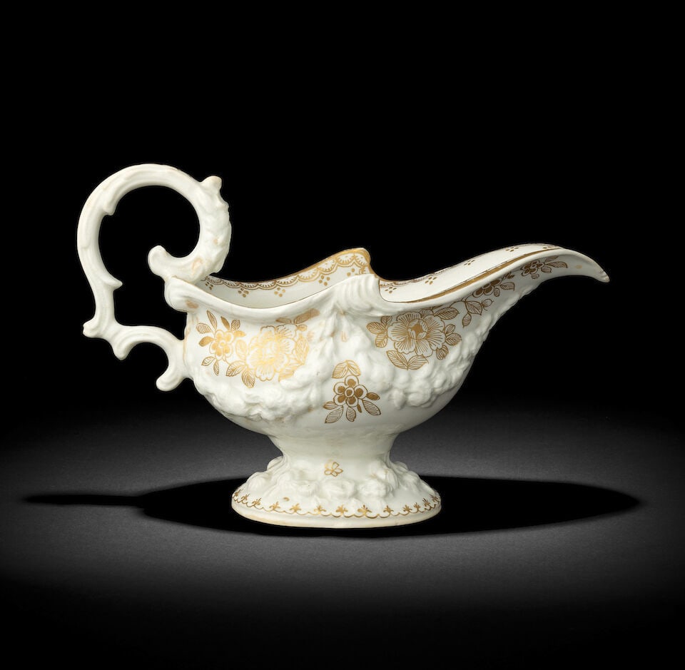 An early Bow sauceboat, circa 1750: An early Bow sauceboat, circa 1750 Of oval shape with a pronounced lip and an elaborate scrolled handle, the body and foot moulded in high relief with floral festoons, decorated with gilt flower spray