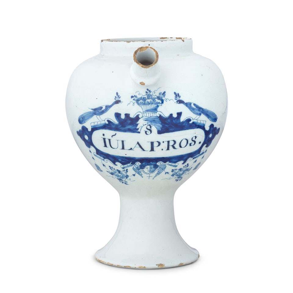 A Dutch Delftware syrup jar, 18th century: A Dutch Delftware syrup jar, 18th century With a globular body on a wide splayed foot, decorated with fruit basket flanked by two peacocks surmounting a label, 'S:IULAP:ROS.', a winged mask below,