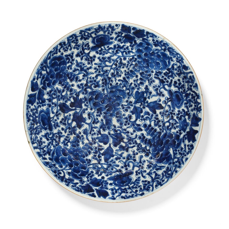 A Kangxi porcelain dish for the Persian market China, 17th/ 18th Century: A Kangxi porcelain dish for the Persian market China, 17th/ 18th Century of shallow rounded form on a short foot, decorated in cobalt-blue on a white ground with chrysanthemums on a ground of floral a