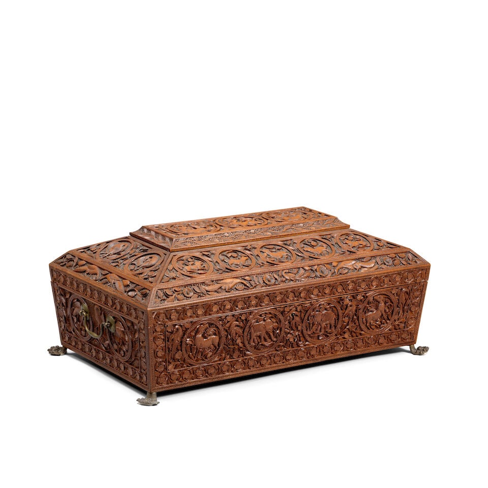 A large Mysore sandalwood casket South India, 19th Century: A large Mysore sandalwood casket South India, 19th Century of sarcophagus form on four brass claw feet with hinged lid, profusely carved with roundels containing animals all on a ground of vegetal int