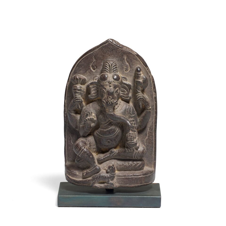 A black stone figure of Ganesh North East India, 11th/ 12th Century: A black stone figure of Ganesh North East India, 11th/ 12th Century Ganesh is seated in royal ease, his pendent foot resting on his vehicle, the rat, his four arms holding a radish, axe, rosary and bo