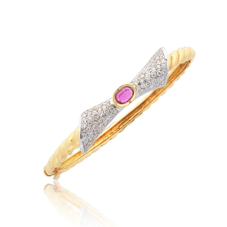 RUBY AND DIAMOND BOW BANGLE, 1988: RUBY AND DIAMOND BOW BANGLE, 1988 Oval-cut ruby Brilliant-cut diamonds approx. 1.65cts total 18 carat gold UK import mark Inner circumference 16.0cm Weight approx. 19.5g Footnotes: OVERALL CONDITION 1