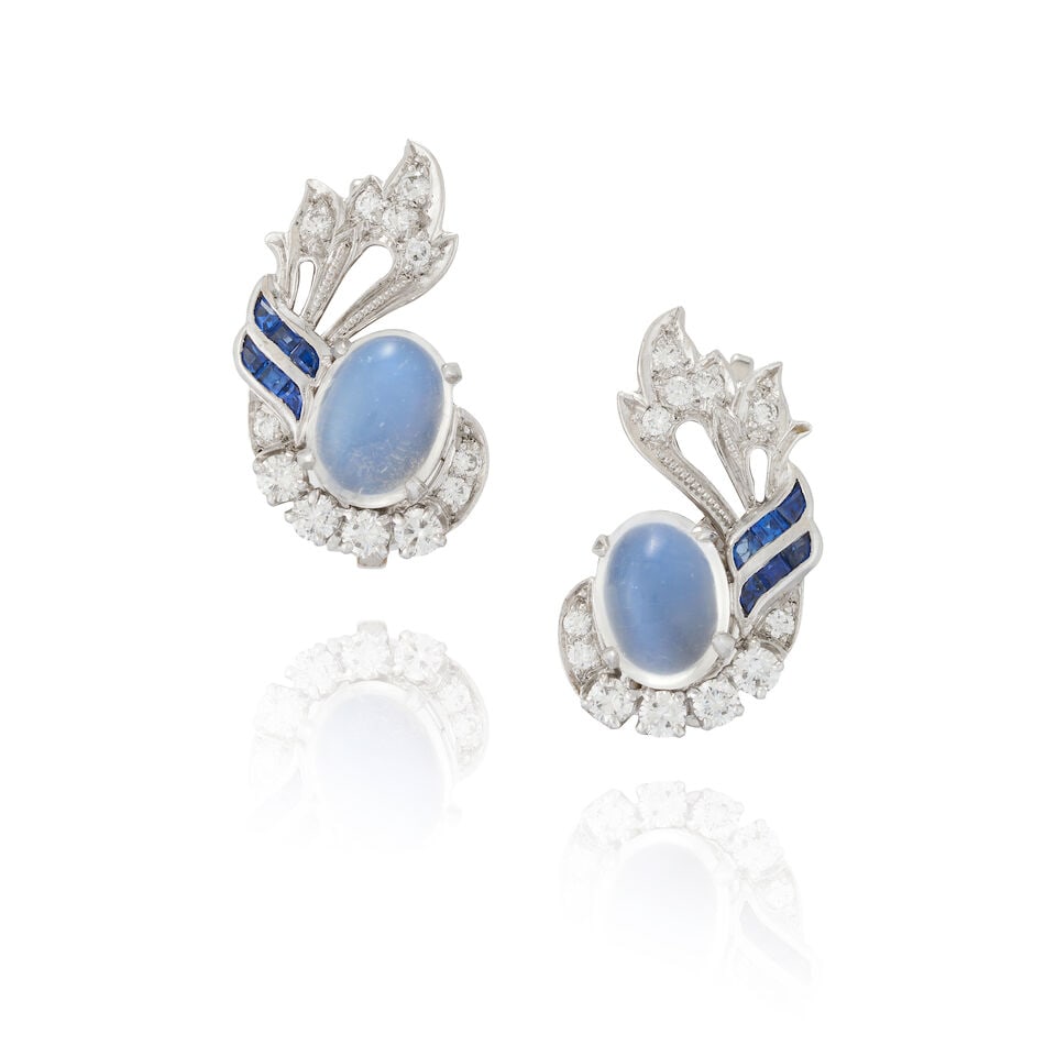 A PAIR OF PLATINUM, MOONSTONE, SAPPHIRE, AND DIAMOND EARCLIPS, CIRCA 1950: A PAIR OF PLATINUM, MOONSTONE, SAPPHIRE, AND DIAMOND EARCLIPS, CIRCA 1950 Each set with an oval cabochon moonstone, surmounted by a spray of full-cut diamonds and channel-set sapphires, weight 8.4