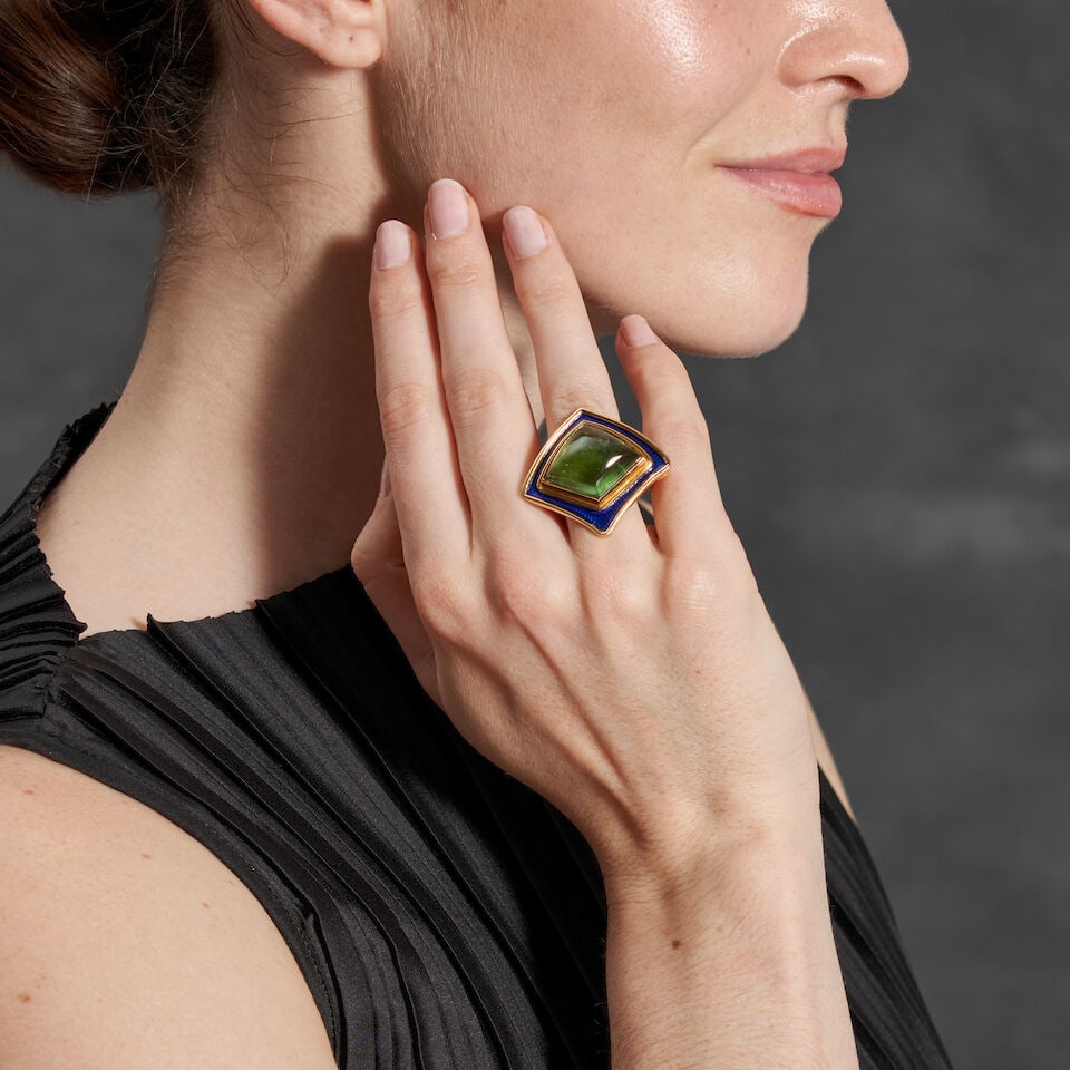 ELIZABETH GAGE: AN 18K GOLD, ENAMEL, AND TOURMALINE RING, ENLAND: ELIZABETH GAGE: AN 18K GOLD, ENAMEL, AND TOURMALINE RING, ENLAND Centering an kite-shaped cabochon tourmaline measuring approximately 29.00 x 18.90 x 8.85 mm, bezel-set within a blue enamel border, we