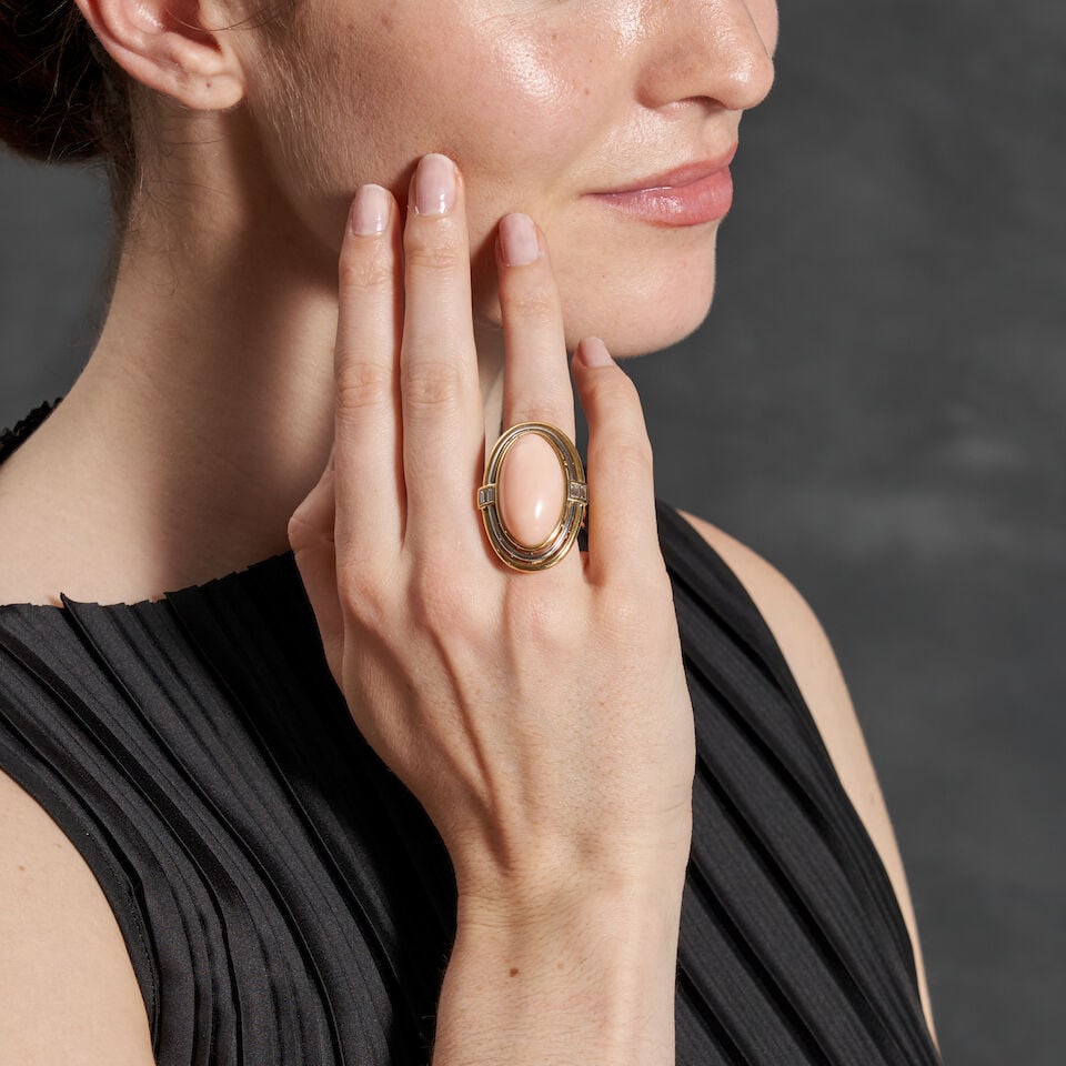 AN 18K BI-COLOR GOLD, CORAL, AND DIAMOND RING: AN 18K BI-COLOR GOLD, CORAL, AND DIAMOND RING Centering a bezel-set oval cabochon coral measuring approximately 27.00 x 15.10 x 8.15 mm, with channel-set baguette-cut diamond accents, weight 16.7 dwt,