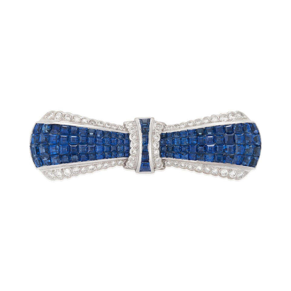 AN 18K WHITE GOLD, SAPPHIRE, AND DIAMOND BROOCH: AN 18K WHITE GOLD, SAPPHIRE, AND DIAMOND BROOCH Designed as a bow with channel-set step, and calibré-cut sapphires, bordered by full-cut diamonds, weight 10.0 dwt, length 2 1/16 in. For