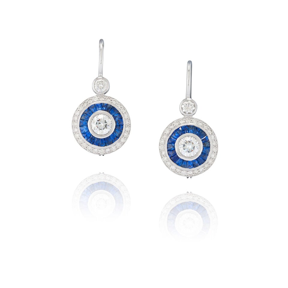 A PAIR OF 14K WHITE GOLD, SAPPHIRE, AND DIAMOND EARRINGS: A PAIR OF 14K WHITE GOLD, SAPPHIRE, AND DIAMOND EARRINGS Each centering a bezel-set full-cut diamond, bordered by channel-set calibré-cut sapphires, and full-cut diamonds, approximate total diamo