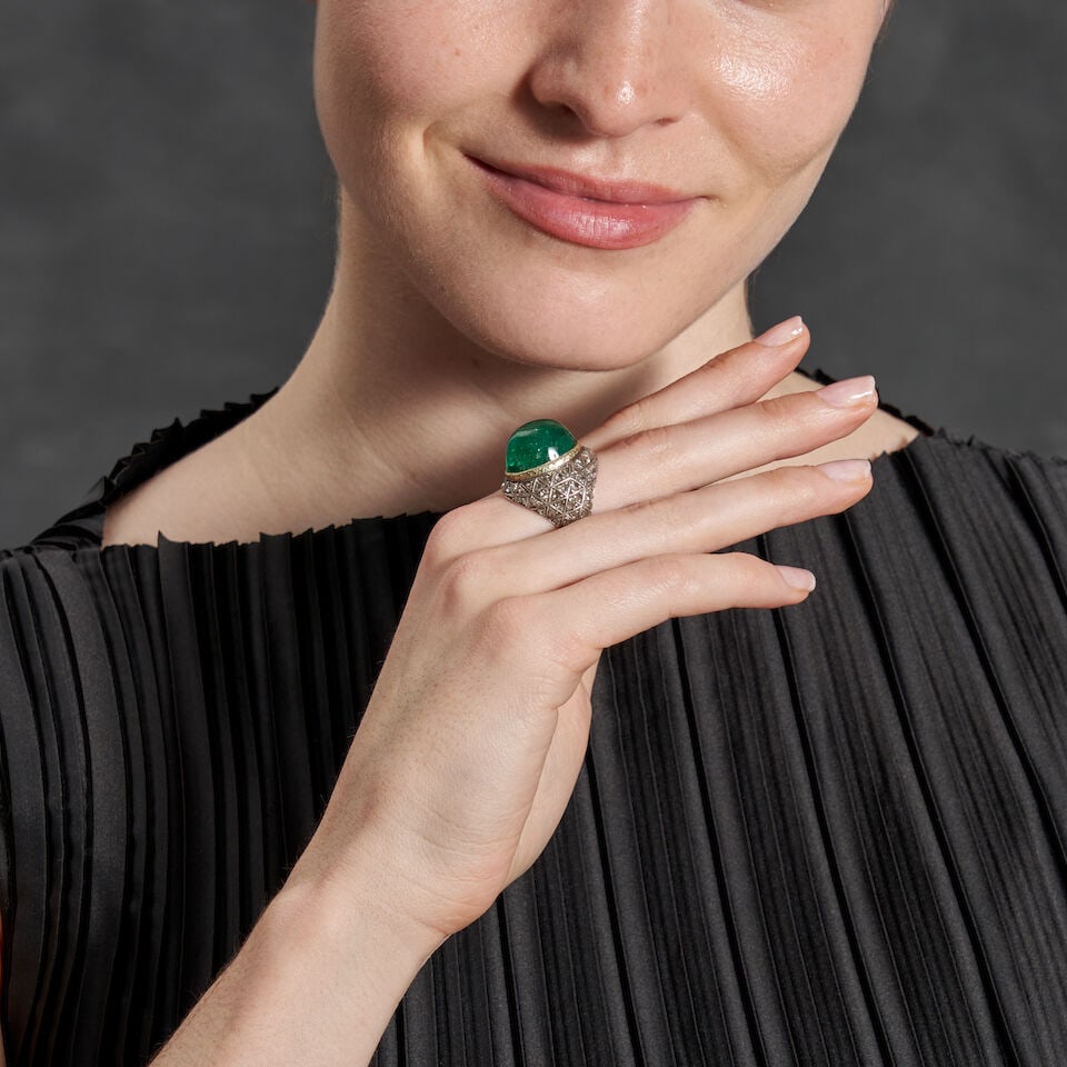 AN EMERALD AND DIAMOND DOME RING: AN EMERALD AND DIAMOND DOME RING Centering a large oval cabochon emerald, measuring approximately 18.20 x 14.80 x 11.10 mm, bezel-set and framed by rose-cut diamonds, in gold and silver, weight 10.8