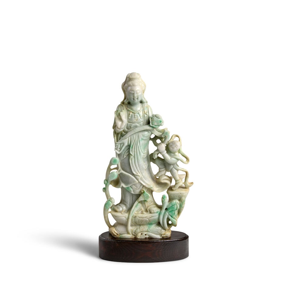 A CREAMISH-GREEN JADEITE GUANYIN WITH A CHILD 19th/20th century: A CREAMISH-GREEN JADEITE GUANYIN WITH A CHILD 19th/20th century 10 7/8in (27.6cm), wood stand Footnotes: 十九/二十世紀 翠玉觀音童
