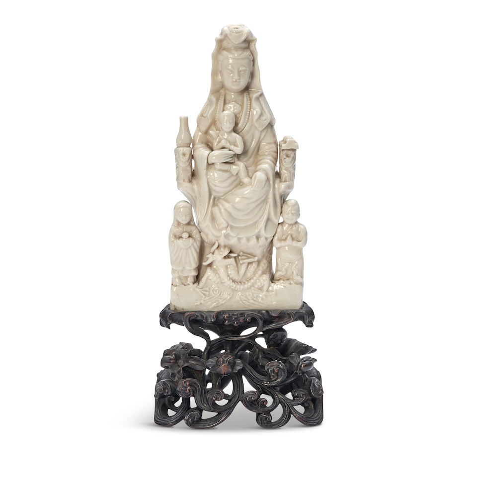 A DEHUA SEATED GUANYIN AND CHILD WITH ATTENDANTS GROUP 17th century: A DEHUA SEATED GUANYIN AND CHILD WITH ATTENDANTS GROUP 17th century Mounted on a carved openwork hardwood stand. 12 1/4in (31.1cm) high, overall Footnotes: 十七世紀 德