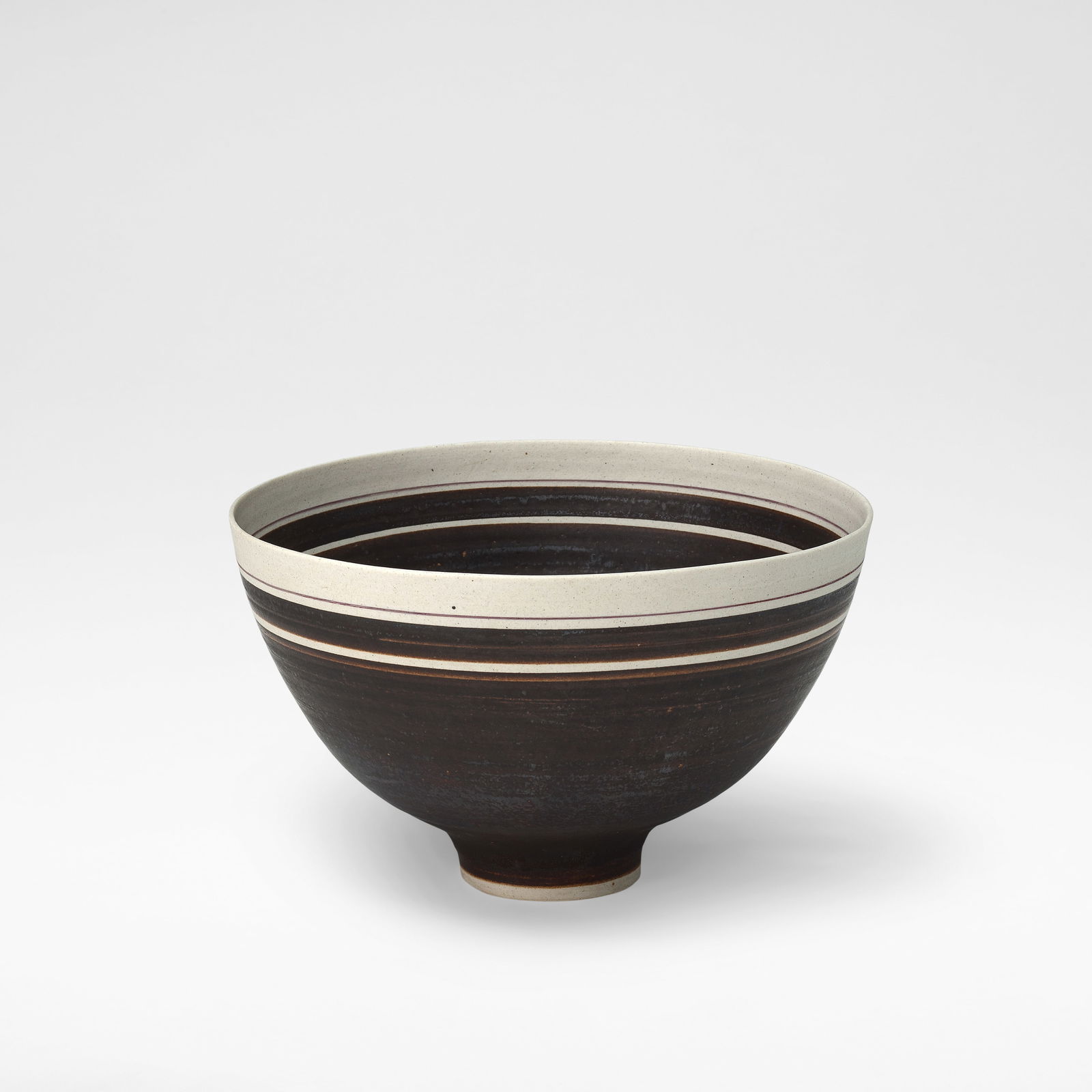 Lucie Rie Footed bowl, circa 1965: Lucie Rie Footed bowl, circa 1965 Porcelain, alternating manganese and unglazed banding with single thin inlaid band near rim. 12 cm high, 19.5 cm diameter Underside impressed with artist's seal. This