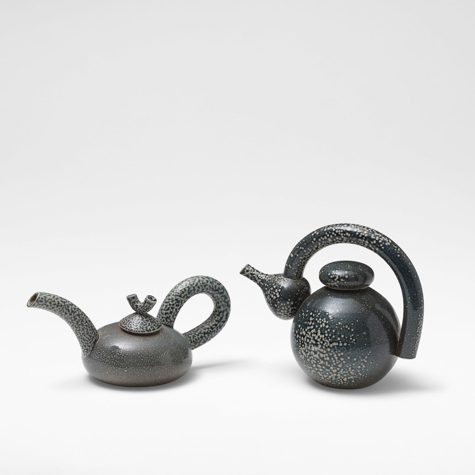 Walter Keeler 'Round Teapot', circa 1982, and 'Macaroni Teapot', circa 1989: Walter Keeler 'Round Teapot', circa 1982, and 'Macaroni Teapot', circa 1989 Stoneware, deep blue and grey salt glazes with running olive green and brown salt glazes to the interiors. Mounted with exag