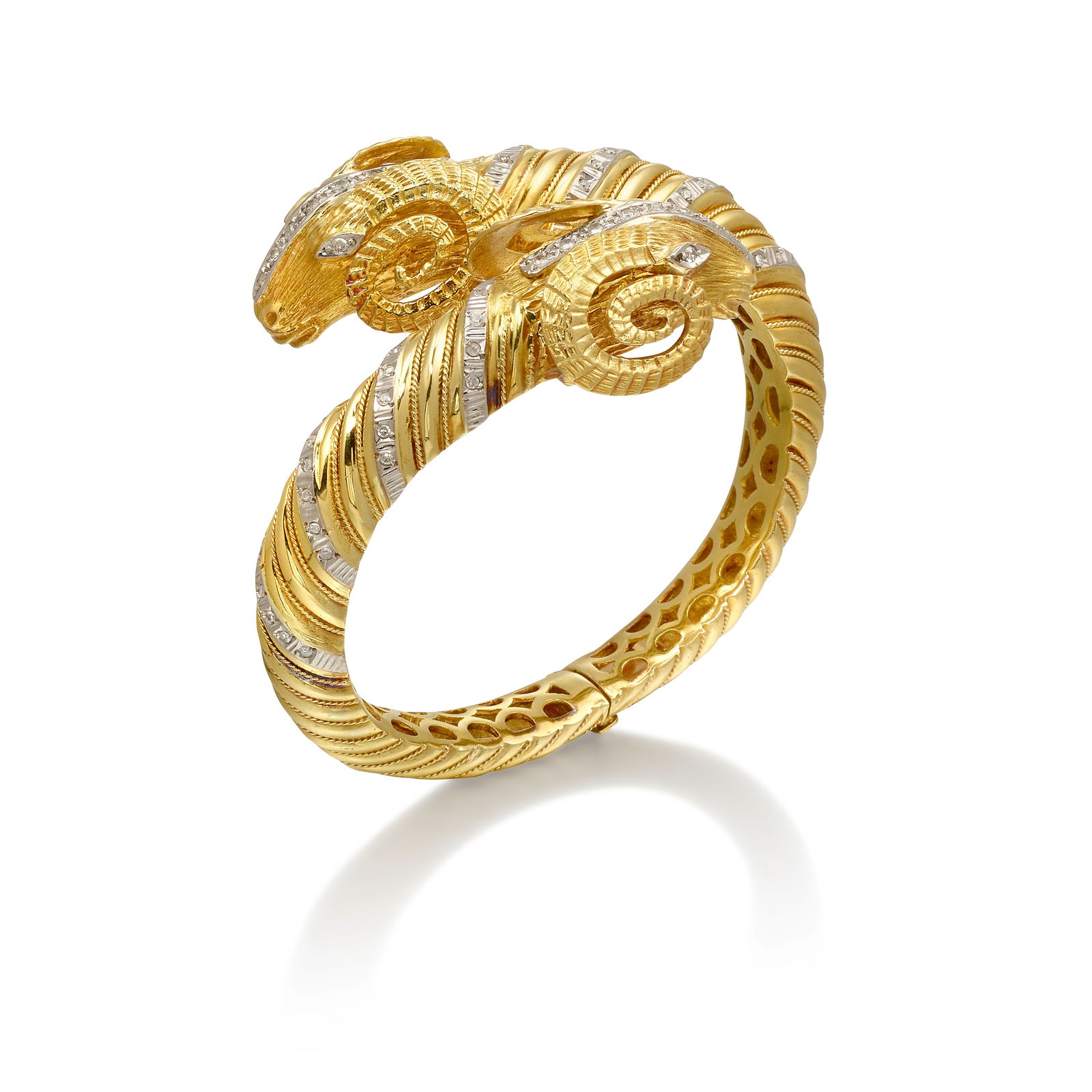 AN 18K BICOLOR GOLD AND DIAMOND BRACELET: AN 18K BICOLOR GOLD AND DIAMOND BRACELETA hinged bangle of bypass design, with ram's head terminals, accented with single-cut diamonds; with partial assay mark; estimated total weight 0.90 carat;