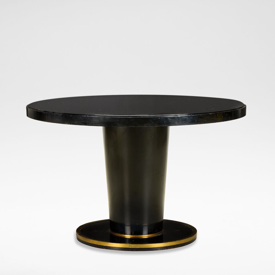 Jean Pascaud Dining table, circa 1930: Jean Pascaud Dining table, circa 1930 Ebonised wood, the circular top with a black glass insert, raised on a flaring column base, terminating onto a brass banded circular foot. 75 cm high, 120 cm