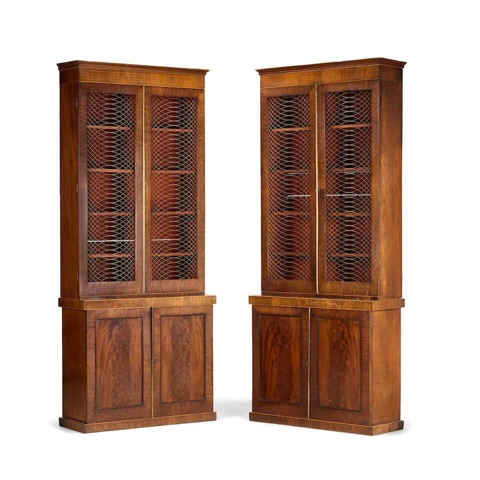 A pair of late George III or Regency mahogany and rosewood library bookcases 1795-1810 (2): A pair of late George III or Regency mahogany and rosewood library bookcases 1795-1810 Each with boxwood line-inlay and stringing, the cavetto cornice above a pair of interlaced brass wirework inset p