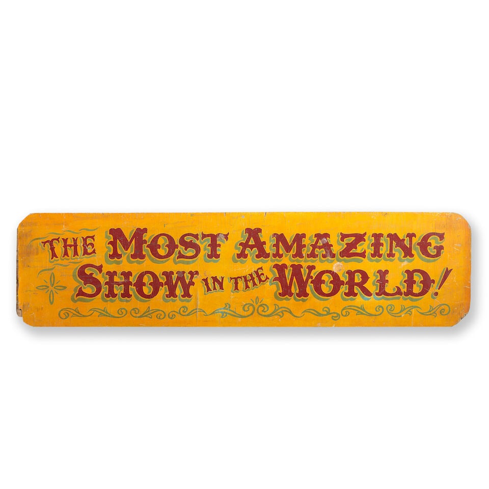 A mid-20th century painted plywood circus sign titled 'The Most Amazing Show In The World!': A mid-20th century painted plywood circus sign titled 'The Most Amazing Show In The World!' The rounded rectangular sign in dark red-brown capital letters shadow-lined in green below a matching green