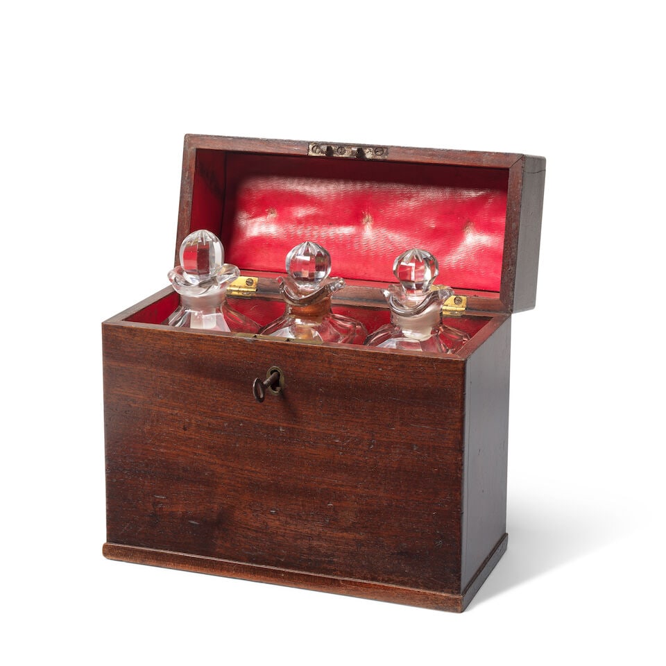 A late George III mahogany cased decanter box Late 18th century: A late George III mahogany cased decanter box Late 18th century The hinged lid with brass carrying handle enclosing three glass decanters engraved 'HOLLANDS', 'BRANDY' and 'RUM', 24cm wide, 11cm deep,