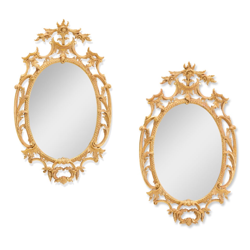 A pair of carved giltwood mirrors 20th century in the George III style (2): A pair of carved giltwood mirrors 20th century in the George III style The oval plates within foliate, C-scroll and icicle carved frames, surmounted by floral crests, 53.5cm wide x 14cm deep x 88.5cm