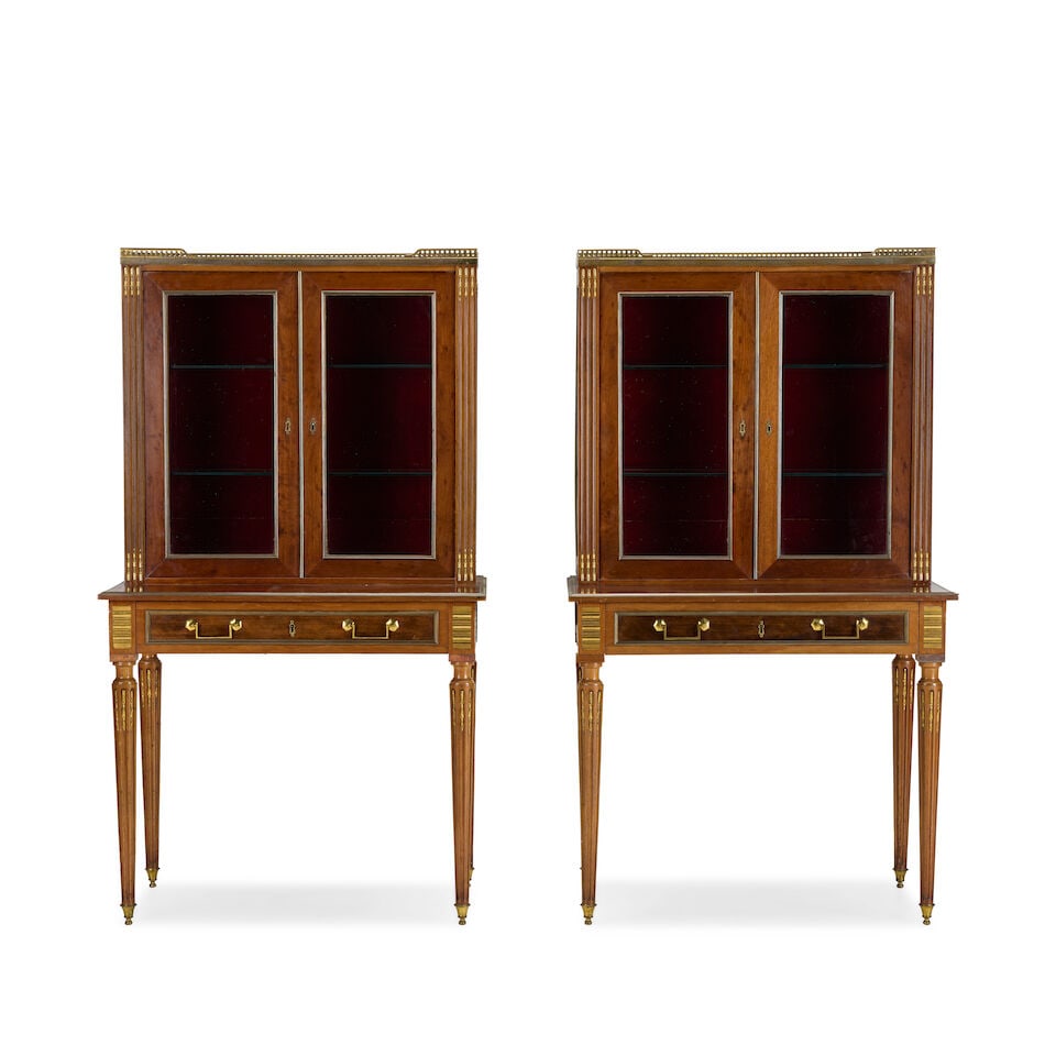 A pair of French mahogany and gilt brass mounted display cabinets on stands Early 20th century i...: A pair of French mahogany and gilt brass mounted display cabinets on stands Early 20th century in the Directoire style The white marble tops with pierced brass three quarter galleries above a pair of