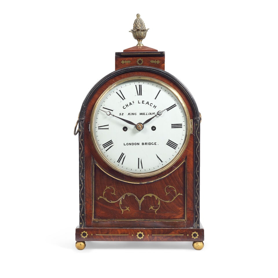 A Regency mahogany and cut brass inlaid bracket clock Charles Leach, London: A Regency mahogany and cut brass inlaid bracket clock Charles Leach, London The arched case surmounted by a pineapple finial, the sides with pierced frets and brass ring handles, the whole raised on f