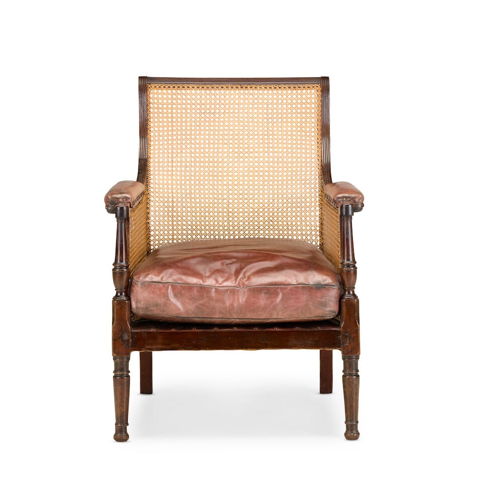 A late Regency mahogany framed library bergèreEarly 19th century: A late Regency mahogany framed library bergère Early 19th century The reeded frame, caned back and sides with leather upholstered armrests and squab cushion, on turned front legs, 68cm wide x 69c