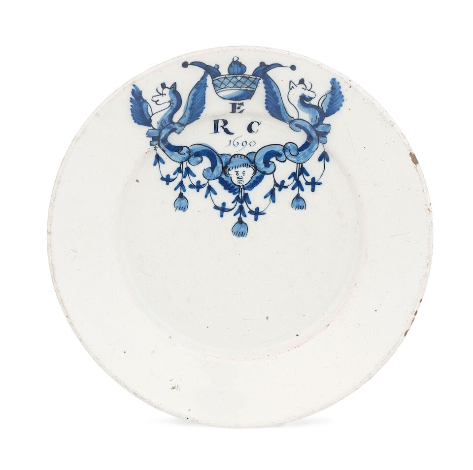 A Dutch Delft plate, dated 1690: A Dutch Delft plate, dated 1690 Probably made for the English market, painted in blue and outlined in black with a crowned scrollwork cartouche flanked by demi-griffins and with an angel head, pendent