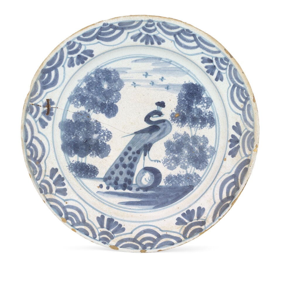 A Dutch delft charger, 18th century: A Dutch delft charger, 18th century Possibly Friesland, painted in blue with a peacock atop a rock, positioned between sponged trees, a formal loop and tassel border, 30.5cm diam For further informati