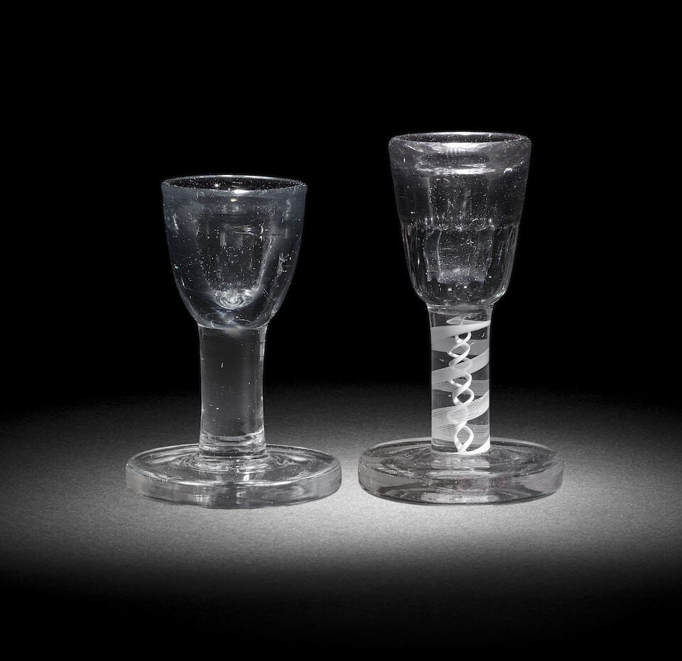 Two deceptive toastmaster's firing or dram glasses, circa 1750-65: Two deceptive toastmaster's firing or dram glasses, circa 1750-65 With thick-walled deceptive round funnel bowls and heavy circular 'firing' feet, comprising a plain stem example, 9.9cm high, an an op