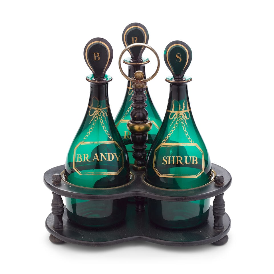 A set of three gilded green glass decanters and stoppers in an ebonised stand, circa 1800-20: A set of three gilded green glass decanters and stoppers in an ebonised stand, circa 1800-20 Of shoulder form, gilt with canted rectangular labels suspende4d from chains and tied ribbons, inscribed 'B